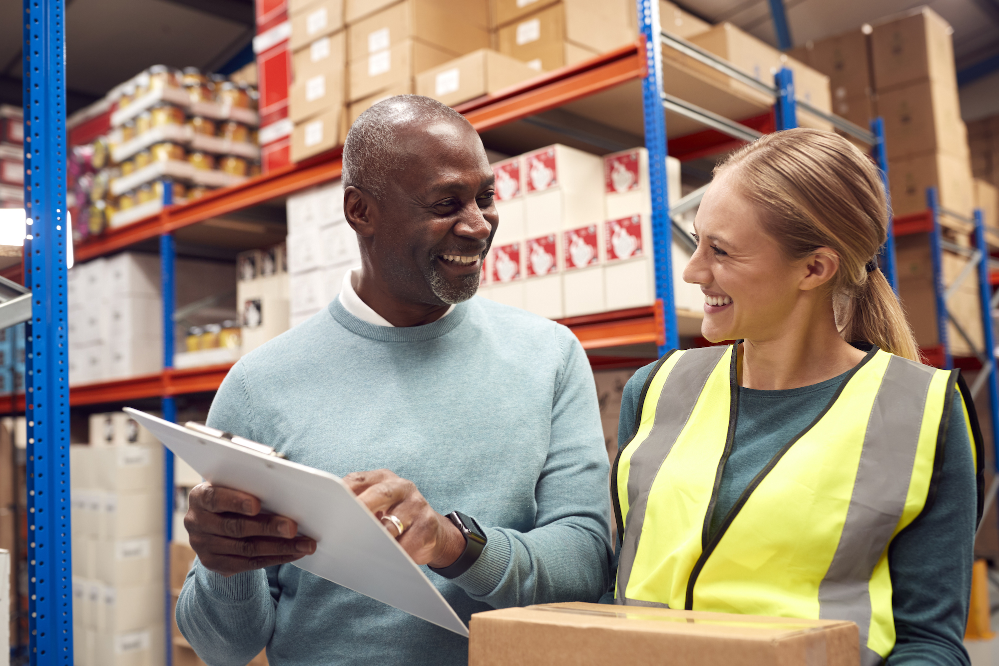 Male Team Leader With Clipboard In Warehouse Training Intern Standing By Shelves